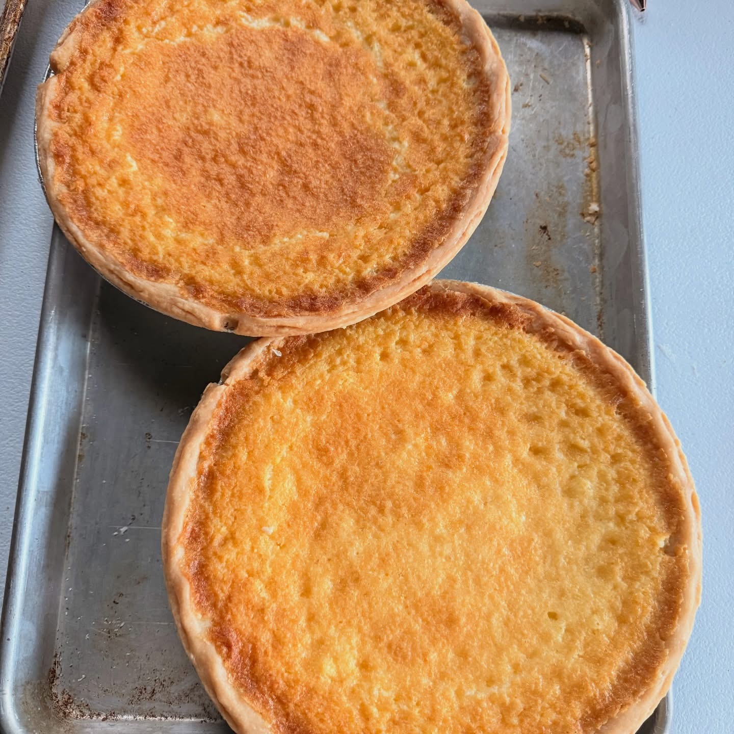 Two golden buttermilk pies cooling on a sheet pan
